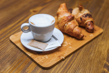 Cup of cappuccino coffee and croissants on a wooden table