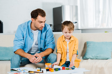 father and preschooler son sitting with art supplies during drawing at home