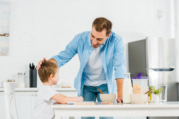 smiling father stroking preschooler son during breakfast in kitchen