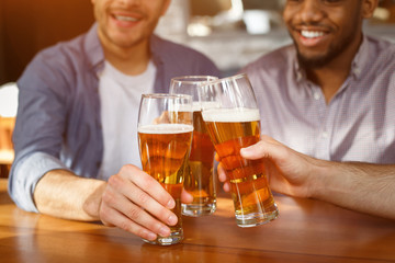 Best friends clinking beer glasses in bar, closeup