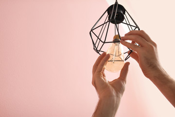 Fototapeta na wymiar Man changing light bulb in lamp on color background. Space for text