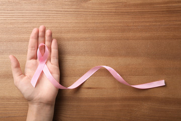 Woman holding pink ribbon on wooden background, top view with space for text. Breast cancer...