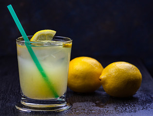 UMO DE LIMÓN EN VASO CON HIELO Y DOS LIMONES SOBRE FONDO OSCURO