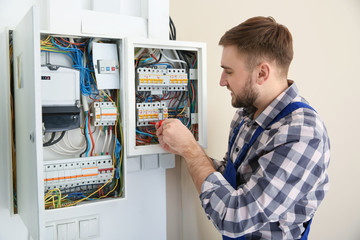 Electrician repairing fuse box with screwdriver indoors