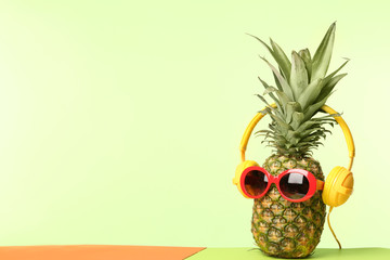 Funny pineapple with headphones and sunglasses on color background, space for text