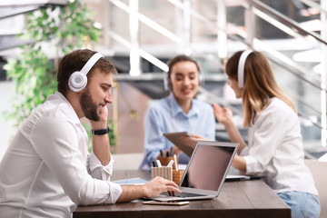 Young businessman with headphones, laptop and his colleagues at table in office