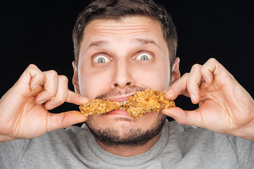 emotional man eating chicken nuggets while looking at camera isolated on black