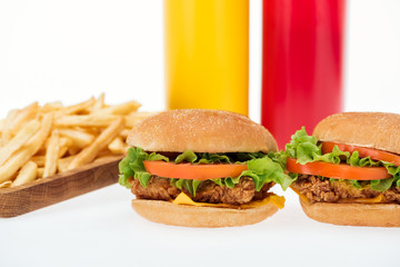 selective focus of tasty chicken burgers near french fries and bottles isolated on white