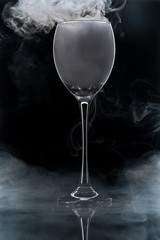 Closeup glass with white fog at dark background. Chemical reaction of dry ice with water.