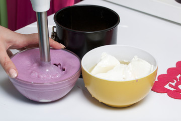 Blueberry cheesecake. A woman mixes blender blueberry jam into cottage cheese jelly. Ingredients for cooking are located on the surface of the table.