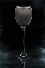Closeup glass with white fog at dark background. Chemical reaction of dry ice with water.