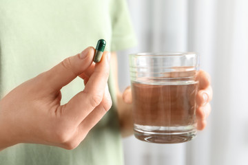 Woman holding spirulina pill and glass of water, closeup