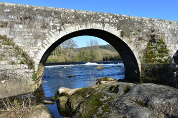Forest, river and waterfall under a medieval stone arch bridge with blue sky. Ponte Maceira, Coruna, Spain.