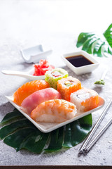Various sushi on ceramic plate with metal Korean sticks on light stone background with green leaves, copy space