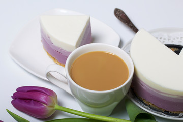 Blueberry cheesecake. A piece of ready-made dessert on a saucer. Jelly layers of different colors are visible. Near a cup of coffee and a bouquet of tulips.
