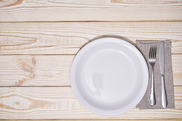 Empty white plate and cutlery on a wooden background, top view.
