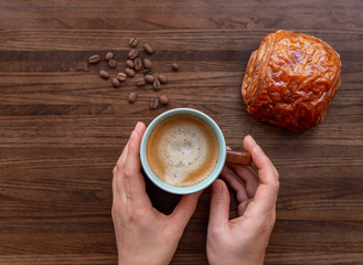 Flat lay, top view, copy space, creative layout. Female hands holding cup of coffee with foam over wooden texture background. Relax with food, coffee break concept. 