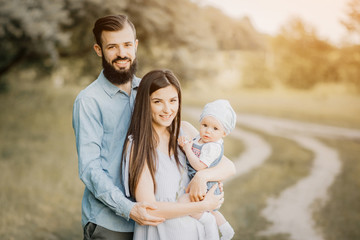 Happy family outdoor in spring. A stylish father with a beard keeps a daughter in his arms with his wife