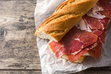 Spanish serrano ham sandwich on wooden table. Copyspace