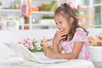 Portrait of little girl sitting at table and using laptop