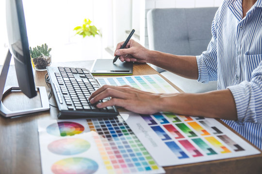 Image of male creative graphic designer working on color selection and drawing on graphics tablet at workplace with work tools and accessories in workspace
