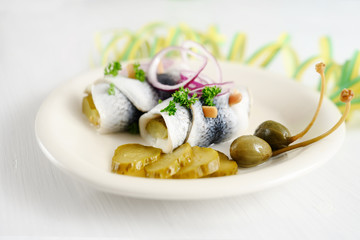 rollmops or rolled pickled herring with red onions, gherkins and capers on a white table with party streamer, a traditional sour hangover breakfast