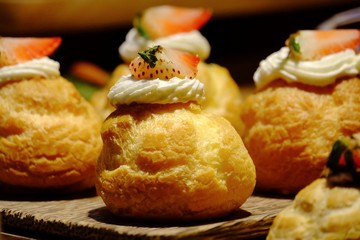 Close up a row of eclair dessert with white cream a piece of fresh strawberry on top on old wooden tray and selling at the wholesale market 