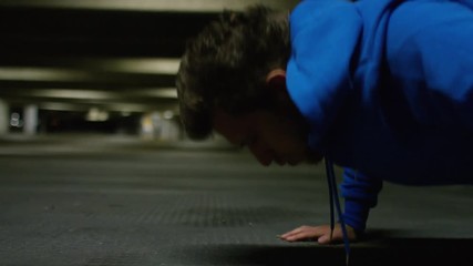 Energetic young man doing push ups in gritty urban venue, in slow motion