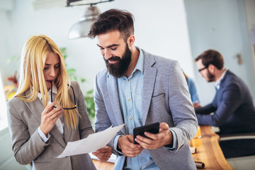 Portrait of two young businesspeople using digital tablet while colleague in background