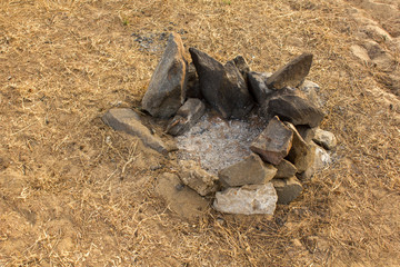 extinct stone campfire with ash on the sand with dry grass