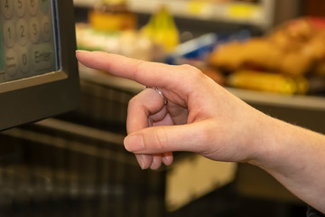 Cashier womans hand using touch screen cash register with groceries on conveyor belt blurred in background -selective focus and bokeh