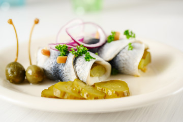 rolled pickled herring, also called rollmops with red onions, gherkins and capers as a hangover meal, close up shot, copy space