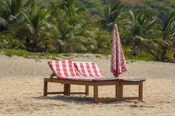 two wooden beach beds with red mattresses and a folded umbrella on the sand against the backdrop of...