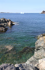 Iceberg close to shore. Twillingate, Newfoundland, Canada. Rugged Rocky cove shoreline in the foreground.