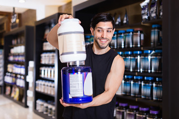 Young attractive muscular man showing his power and holding pot of  sport nutrition