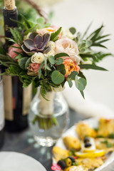 A bouquet of flowers from succulents and roses stands in a vase on the table