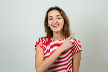 Obraz premium Happy young caucasian female in a striped red T-shirt pointing fingers away, showing copy space for your text.