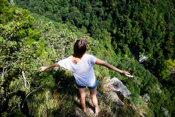 A girl stands on the edge of a mountain cliff spreading her arms