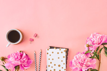 Flat lay blogger or freelancer workspace with a notebook and pink peonies on a pink background