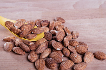 Pile of almonds with yellow spoon on wooden floor.