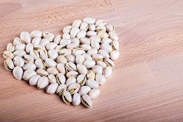 Pistachio nuts forming a heart-shape on wooden floor background