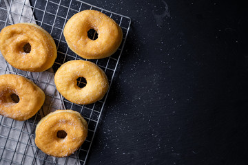 Sweet pieces of sugar doughnuts on wire rack in dark background, top view