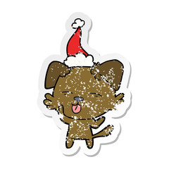 distressed sticker cartoon of a dog sticking out tongue wearing santa hat