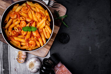 penne pasta with shrimps, tomato sauce   in a black frying pan with spice ,top view.