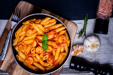 penne pasta with shrimps, tomato sauce   in a black frying pan with spice ,top view.