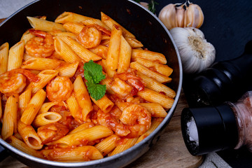 penne pasta with shrimps, tomato sauce   in a black frying pan with spice ,close up