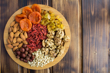 Dried apricots, raisins, goji berries and different nuts on the round cutting board on the brown ...