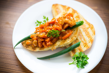fried bread toasts with stewed beans and vegetables in a plate