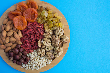 Dried apricots, raisins, goji berries ,different nuts on the round cutting board on the blue background.Top view.Copy space.
