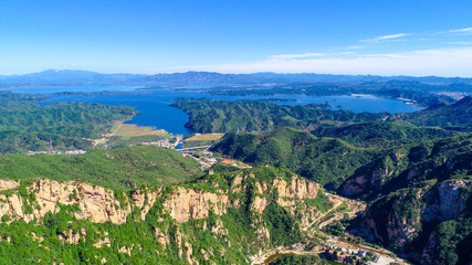 Obraz premium Aerial view of mountain with water reservoir on the background. Mountain peak with beautiful blue sky and green forest. Landscape of mountain in natural reserve park. Miyun, Beijing, China.